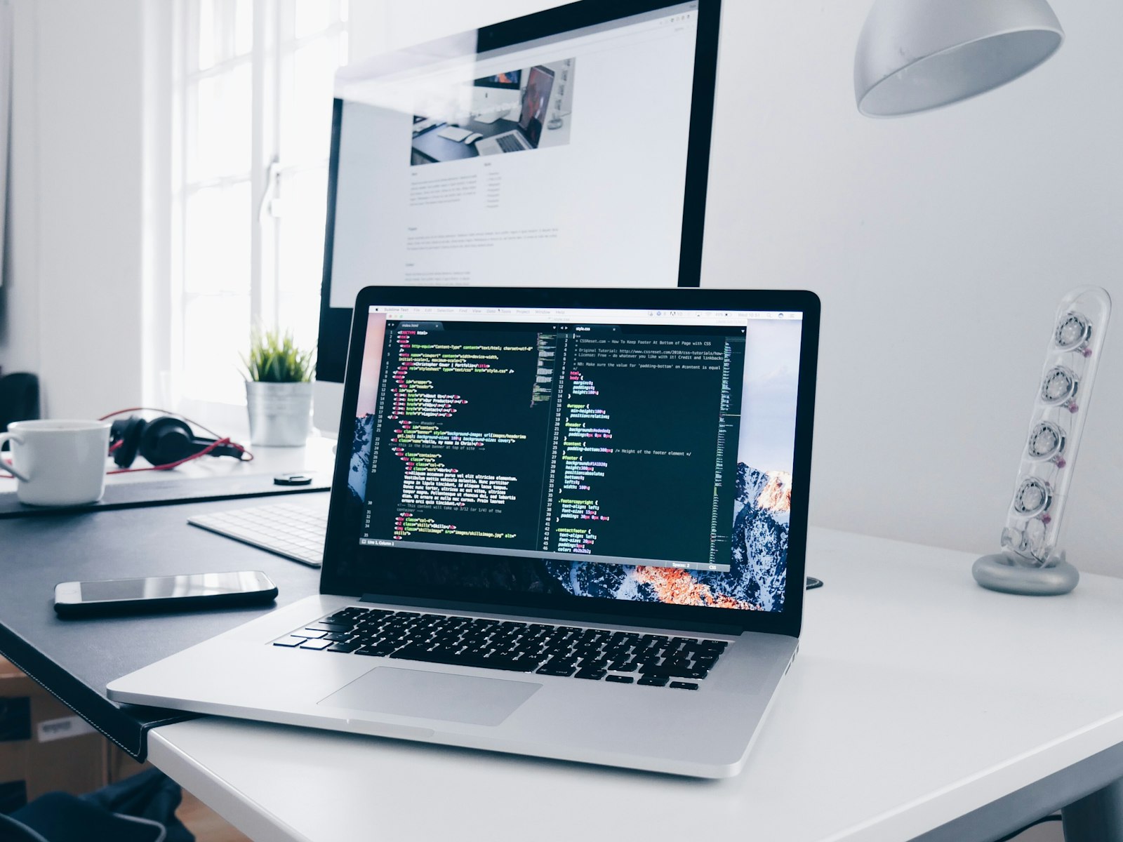 Laptop and monitor on a desk showing website code and design work